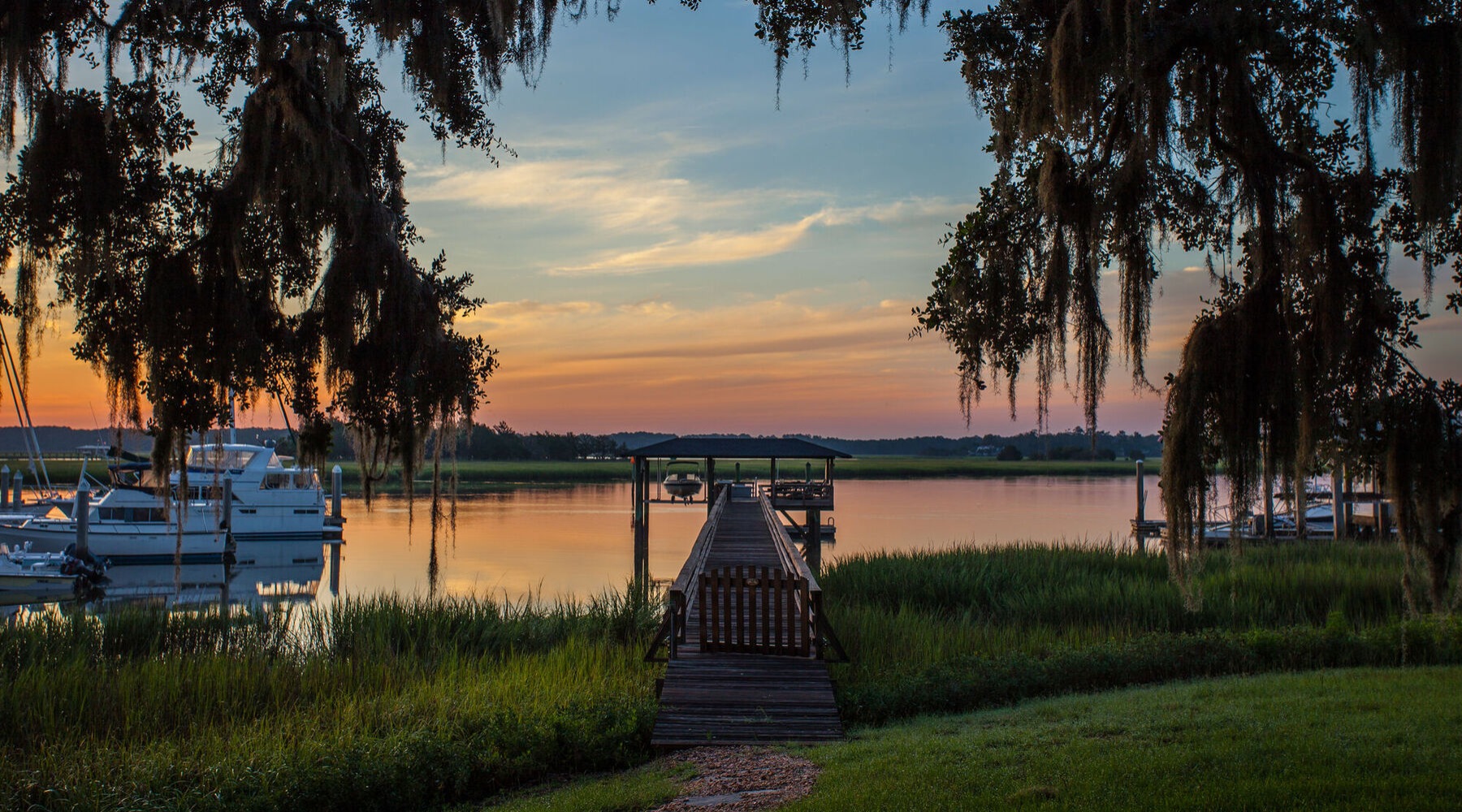 a dock on a bayou at sunset with trees in the foreground
